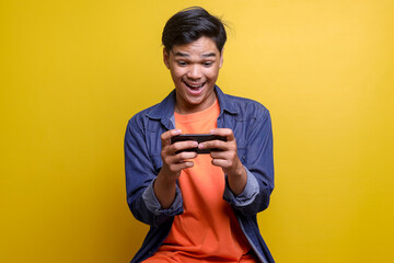 Cheerful young Asian man looking at mobile phone with happy excited expression