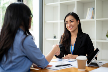 A gorgeous Asian businesswoman is shaking hands with a female client in the office
