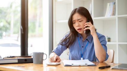 A stressed Asian businesswoman is making a call to her employee to complain about mistakes