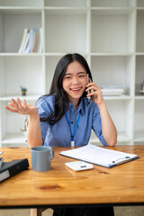 A happy Asian businesswoman enjoys talking on the phone with her friend at her desk