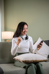 A joyful Asian woman receives good news on the phone, shows her fist, and screams with happiness