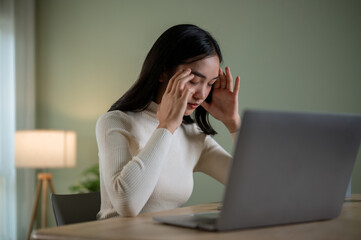 A thoughtful Asian woman is feeling stressed, tired and headache-ridden while working