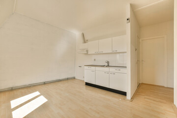 an empty room with wood floors and white cabinets on the wall, there is a small kitchen in the corner