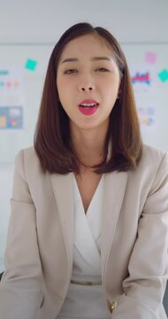 Asian beautiful businesswoman talking to camera with smiling. She sharing about work with team at meeting room. Online work concept.