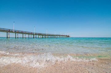 Fototapeta premium view of the pier in El Coromuel beach, on a beautiful and sunny summer morning with clear blue sky and the transparent sea of ​​Cortes. La Paz Baja, seascape of Mexico