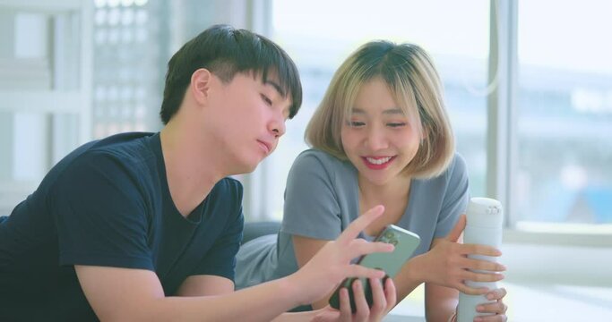 Happy young asian people using phone in living room while breaking from exercise. They exercise at home together.