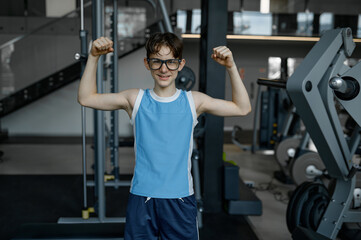 Funny preteen boy child showing arm muscle after training at gym