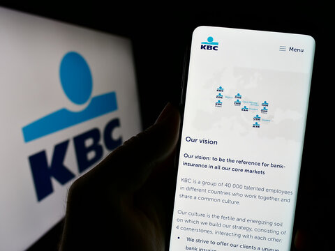 Stuttgart, Germany - 08-26-2023: Person holding cellphone with website of Belgian financial company KBC Group N.V.  on screen in front of logo. Focus on center of phone display.