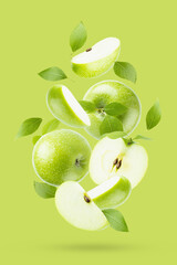 Juicy green apples with green leaves fly as flow on bright green background, closeup, whole, half...