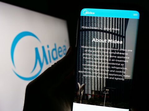 Stuttgart, Germany - 08-28-2023: Person holding cellphone with webpage of Chinese home appliances company Midea Group on screen in front of logo. Focus on center of phone display.