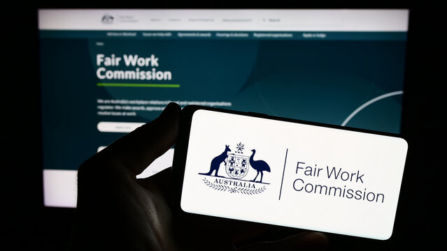 Stuttgart, Germany - 08-28-2023: Person holding smartphone with logo of Australian Fair Work Commission (FWC) on screen in front of website. Focus on phone display.