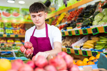 Focused male greengrocer in apron laying out local pomegranates in the fruit shop