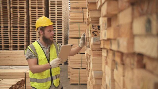 Portrait of warehouse worker checking stock of wooden pallets in storage warehouse.