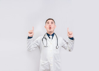 Surprised doctor pointing an advertisement up. Amazed doctor pointing a promotion up. Male doctor looking and pointing up isolated