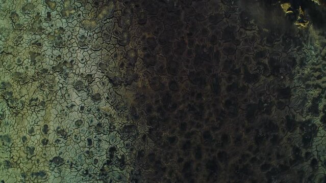 Cracked black spots on barren earth remain from asphalt lake of toxic runoff, golden hour