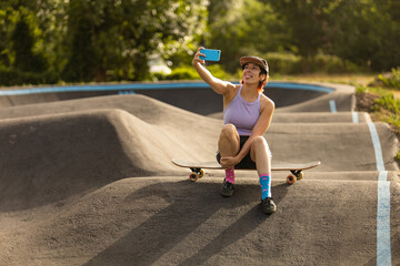 short-haired woman in skatepark practicing sports in the middle of the forest, taking selfies, smiling, making a video call,