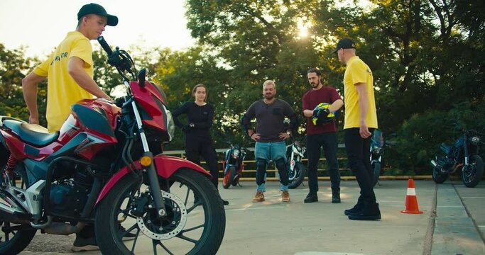 Two instructor guys in a driving school communicate with their students. A group of motorcyclists stand at the driving range along with motorcycles