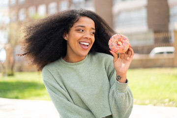 Young African American woman holding a donut at outdoors with happy expression