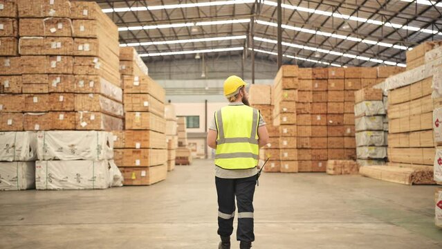 Young man warehouse worker checking stock of wooden pallets in storage warehouse.