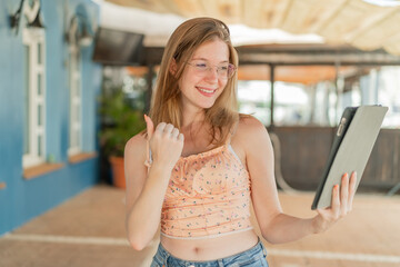 French girl with glasses holding a tablet at outdoors celebrating a victory