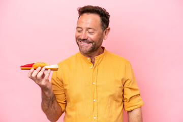 Middle age Caucasian man holding sashimi isolated on pink background looking to the side and smiling