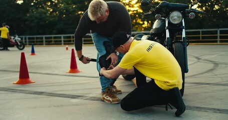 Driving instructor in yellow t-shirt helps young biker put on knee pads. Motorcycle and bike driving instructor