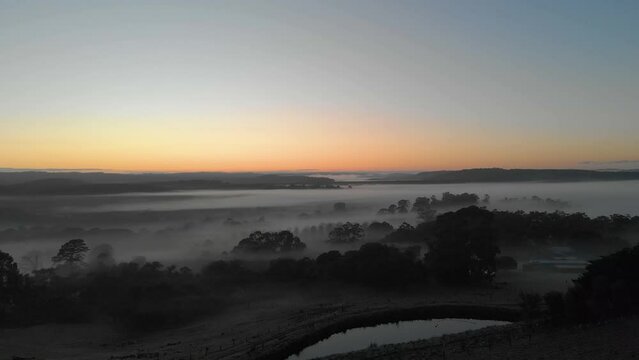 Aerial moving forward low over farm land in Australia with mist and fog over the land in winter.