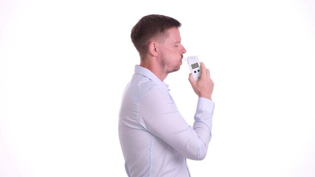 Young male checks blood alcohol level in white studio. Bearded man uses breathalyzer special device for alcohol level in blood slow motion