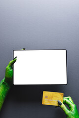 Vertical image of green monster hands with credit card and tablet with copy space on grey background