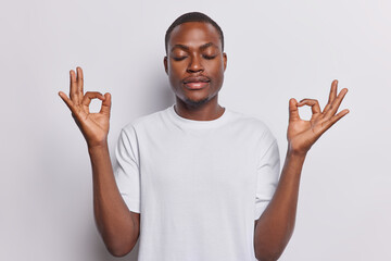 Dark skinned man as he indulges in tranquility of morning yoga with his eyes closed focuses on practicing breathing exercises seeking inner peace and harmony finds balance isolated on white background - 641979777
