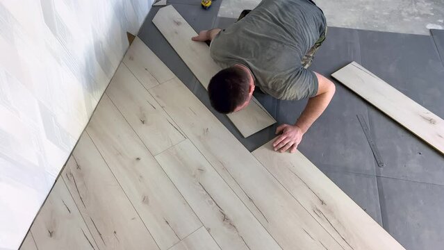 Laying a gray parquet board on the substrate. The work of a builder. A man repairs the floor in the room. The process of laying laminate on a polyurethane substrate. Floor repair. High quality 4k