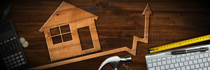 Growth and development of the real estate business concept. Wooden model house on a wooden workbench with uptrend arrow graph, calculator, coins, tape measure, computer keyboard, hammer and copy space