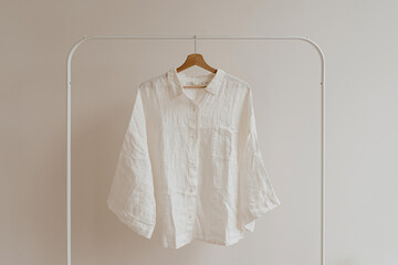 White crumpled shirt, blouse on hanger over white wall. Aesthetic female fashion clothes, wardrobe...