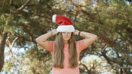 A young woman puts on Santa's red hat in the forest. Christmas in a warm climate.