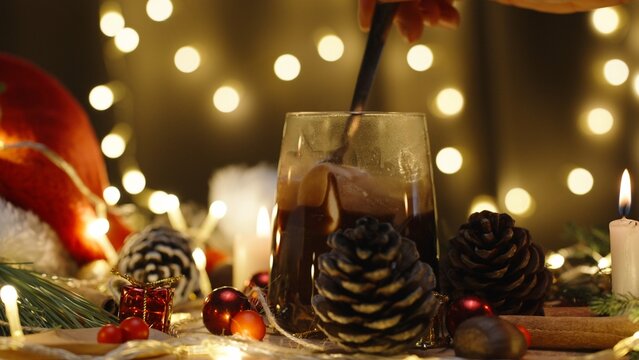 I stir marshmallows in cocoa, hot chocolate on the background of a garland of lights. Christmas table with candles and decorations.