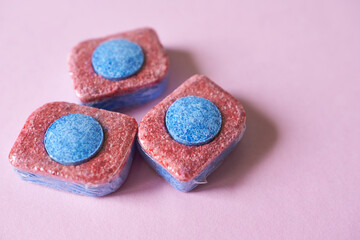 Dishwasher capsules on pink background, closeup. Dishwasher detergent.