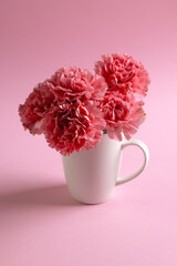 Vertical image of bunch of pink carnation flowers in white mug with copy space on pink background