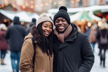 Fototapeten Happy young smiling black couple in winter clothes at street Christmas market in Stockholm © Jasmina