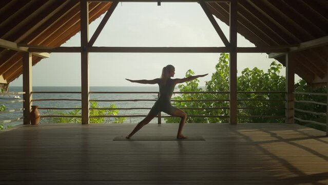 Woman leaning into warrior pose in serene wooden cabana, yoga wellness sanctuary