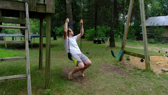 Poor man in barefoot wearing dirty shorts and white shirt gently rocking on swing while trying to ease his mind while being uneasy or concerned for his future.
