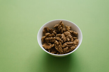 Walnuts on a white plate on a green background. Source of iron, vitamins and minerals