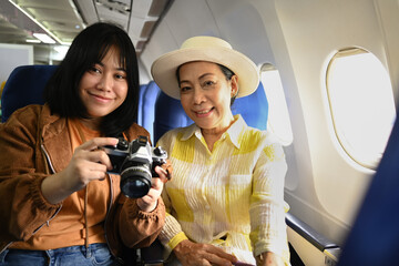 Happy senior woman and daughter sitting in passenger airplane and taking picture, waiting for...