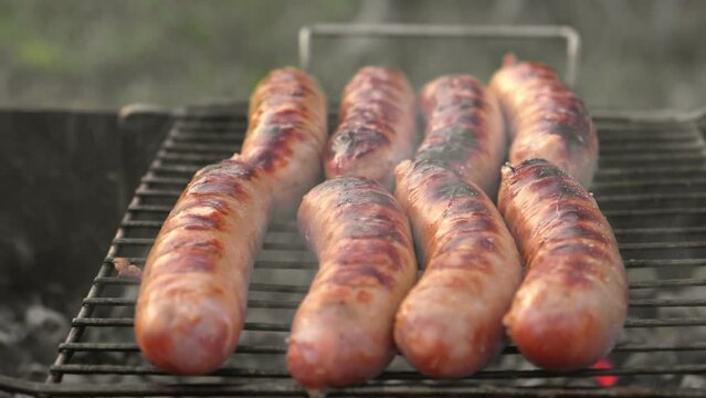 Grilled sausages. Cook man preparing grilling food bbq. Barbecue with smoke, flame outdoors. Tasty juicy german bratwurst. Charcoal kettle grill outside in backyard. Family summer vacation. Close-up	
