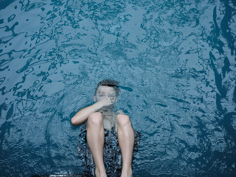 View from above boy swimming, holding breath under water surface
