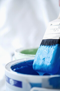 Close up of blue paint pot and dripping paintbrush
