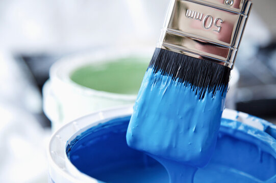 Close up of blue paint pot and dripping paintbrush
