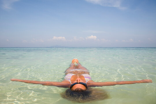 Young woman floating in crystal clear sea water with arms wide open, Koh Phi Phi, Thailand
