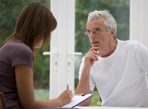 Close up of young woman taking notes from consultation with gray haired man
