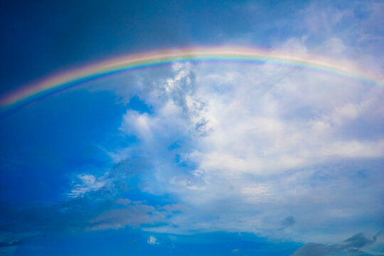 Beautiful multi-colored rainbow after rain on the blue sky and white clouds.
