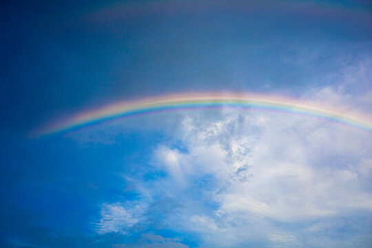 Beautiful multi-colored rainbow after rain on the blue sky and white clouds.